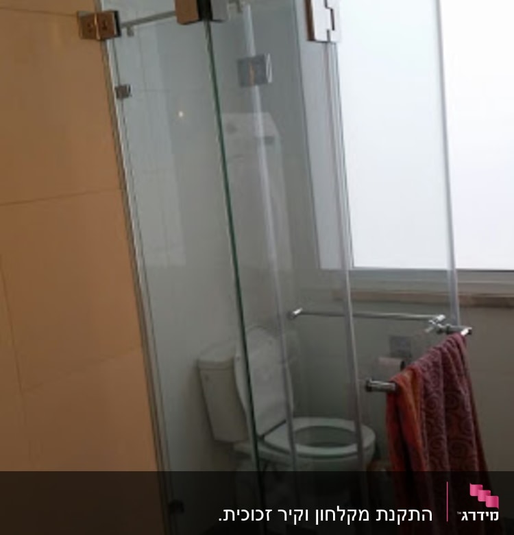 מקלחון זכוכית עם דלתות שקופות ומגבת תלויה